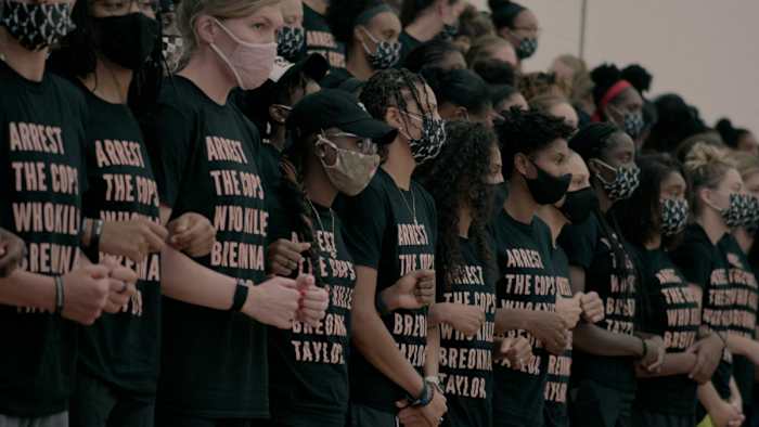 A group of WNBA players wearing black shirts that read "Arrest the cops who killed Breonna Taylor"